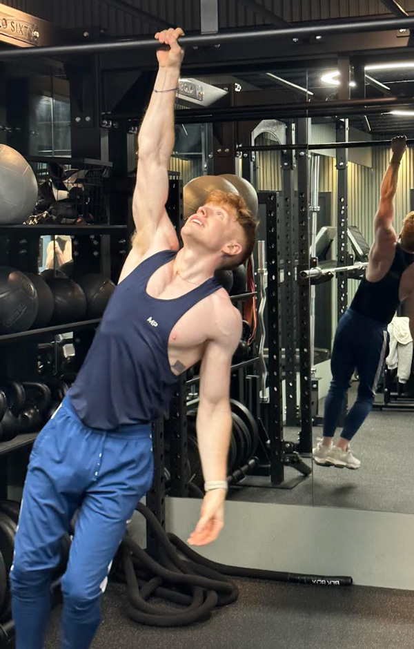 Coach is doing a pull ups with one hand in the gym.